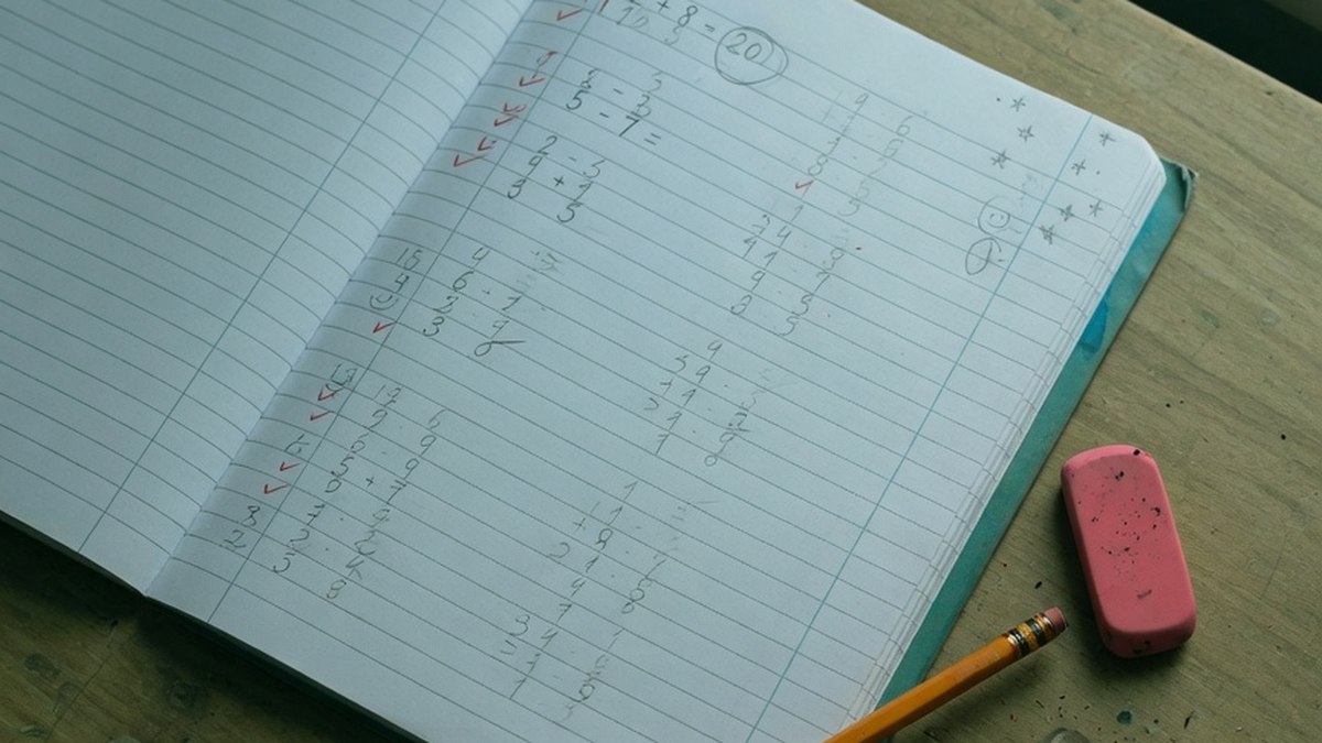 Cahier d'exercices de mathématiques ouvert sur une table en bois, avec un crayon posé à côté, vue de dessus sans personne visible
