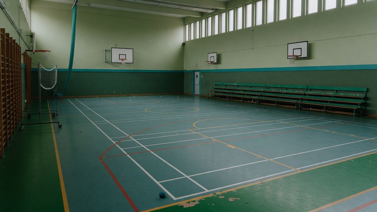 Un terrain de sport scolaire vide avec des lignes tracées au sol, vu de loin, sans personne présente